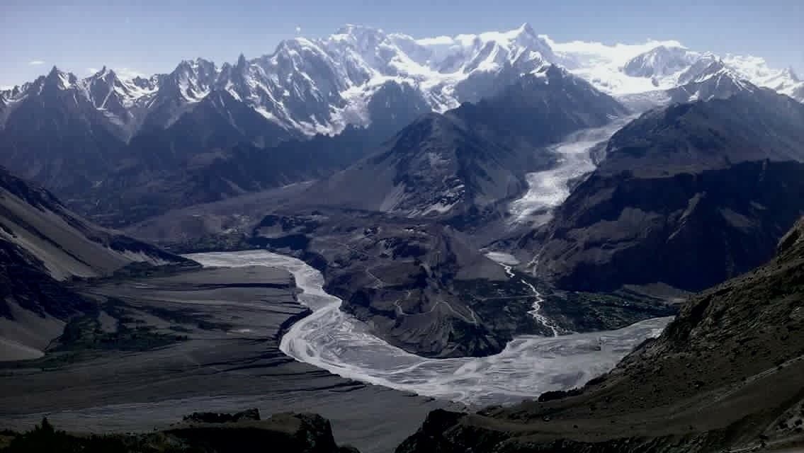 Wide aerial view of a curving glacial river cutting through the Karakoram mountains