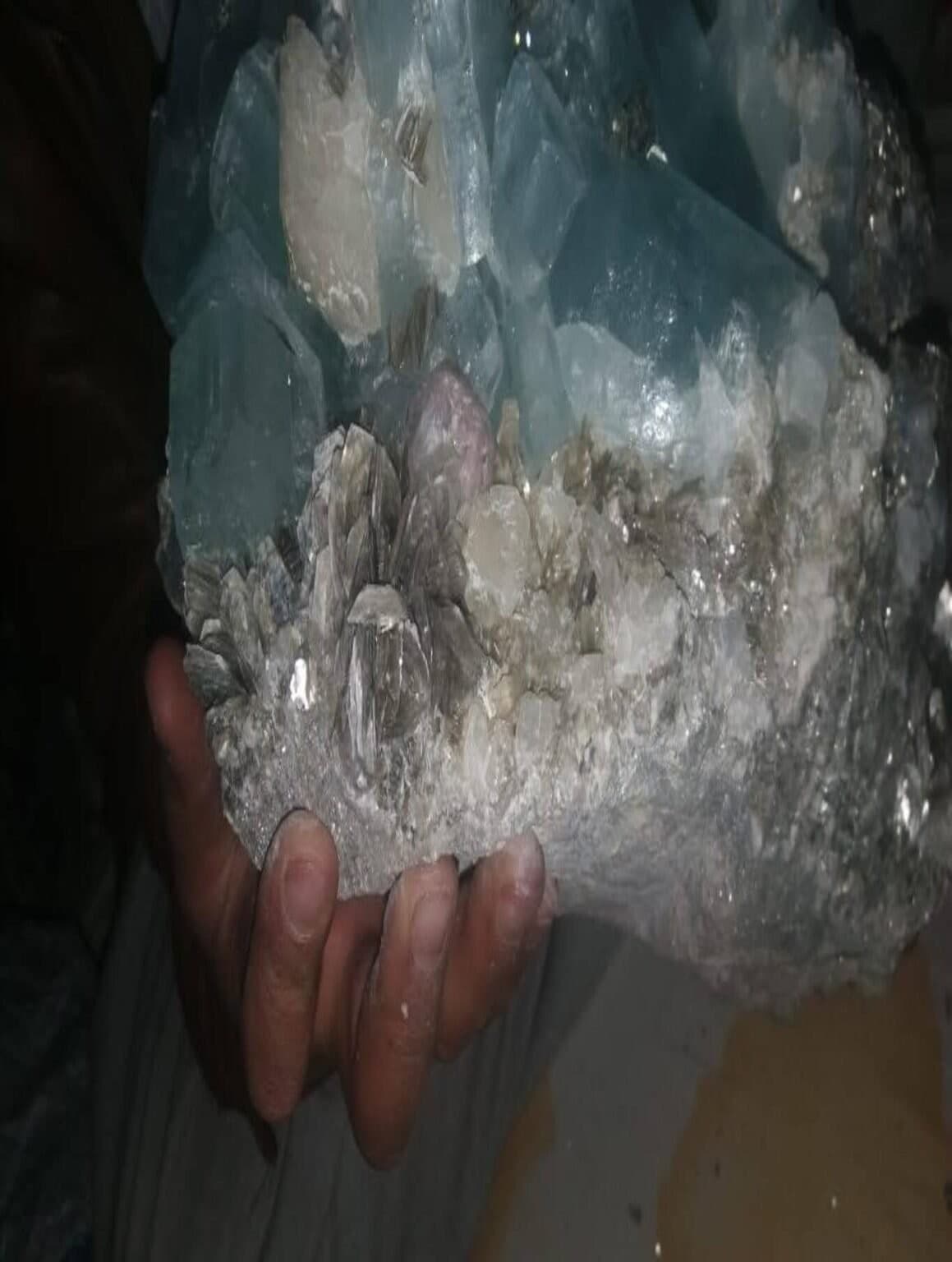 A large aquamarine crystal cluster on matrix held in hand