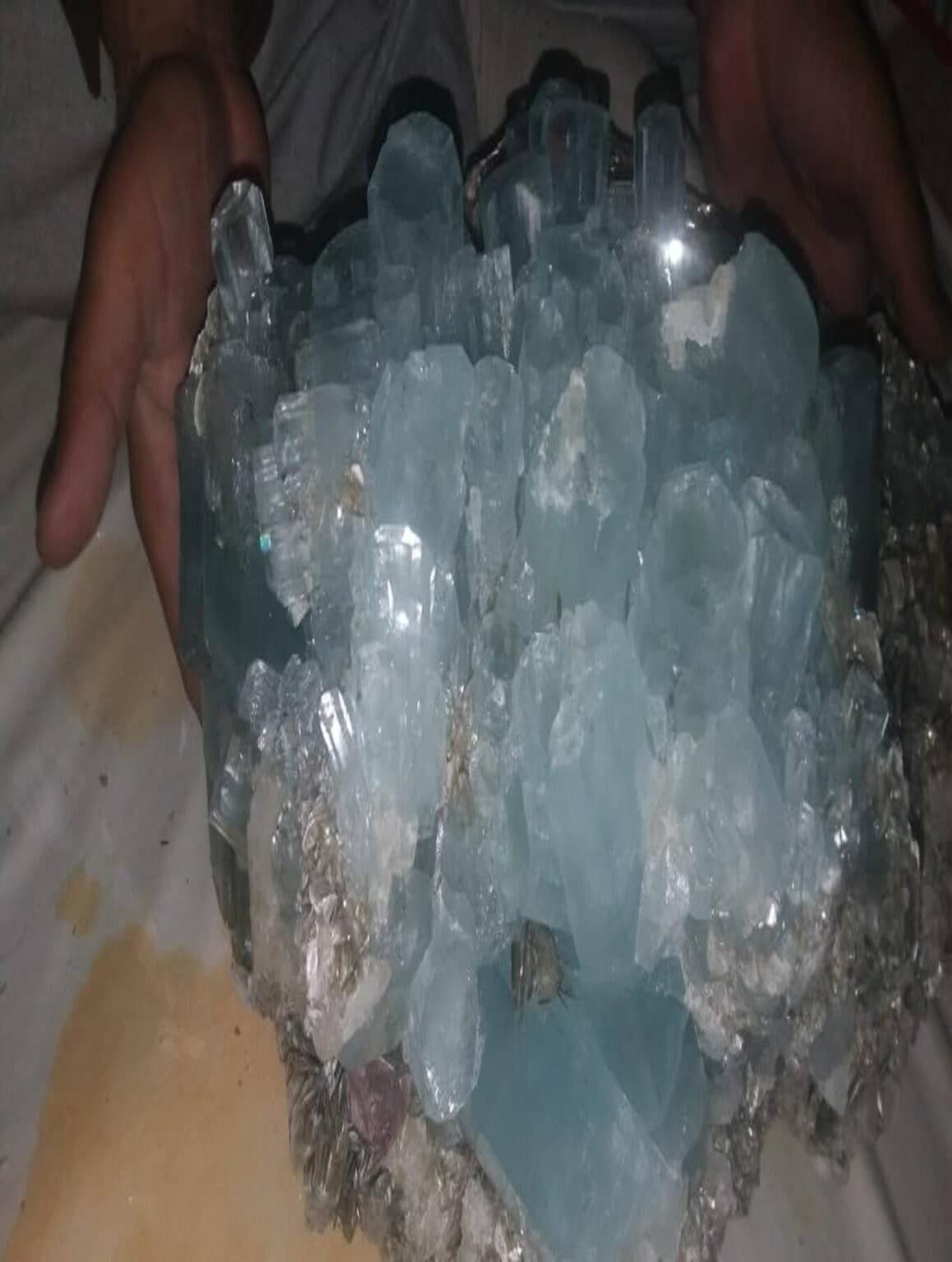 A large aquamarine crystal cluster held with two hands