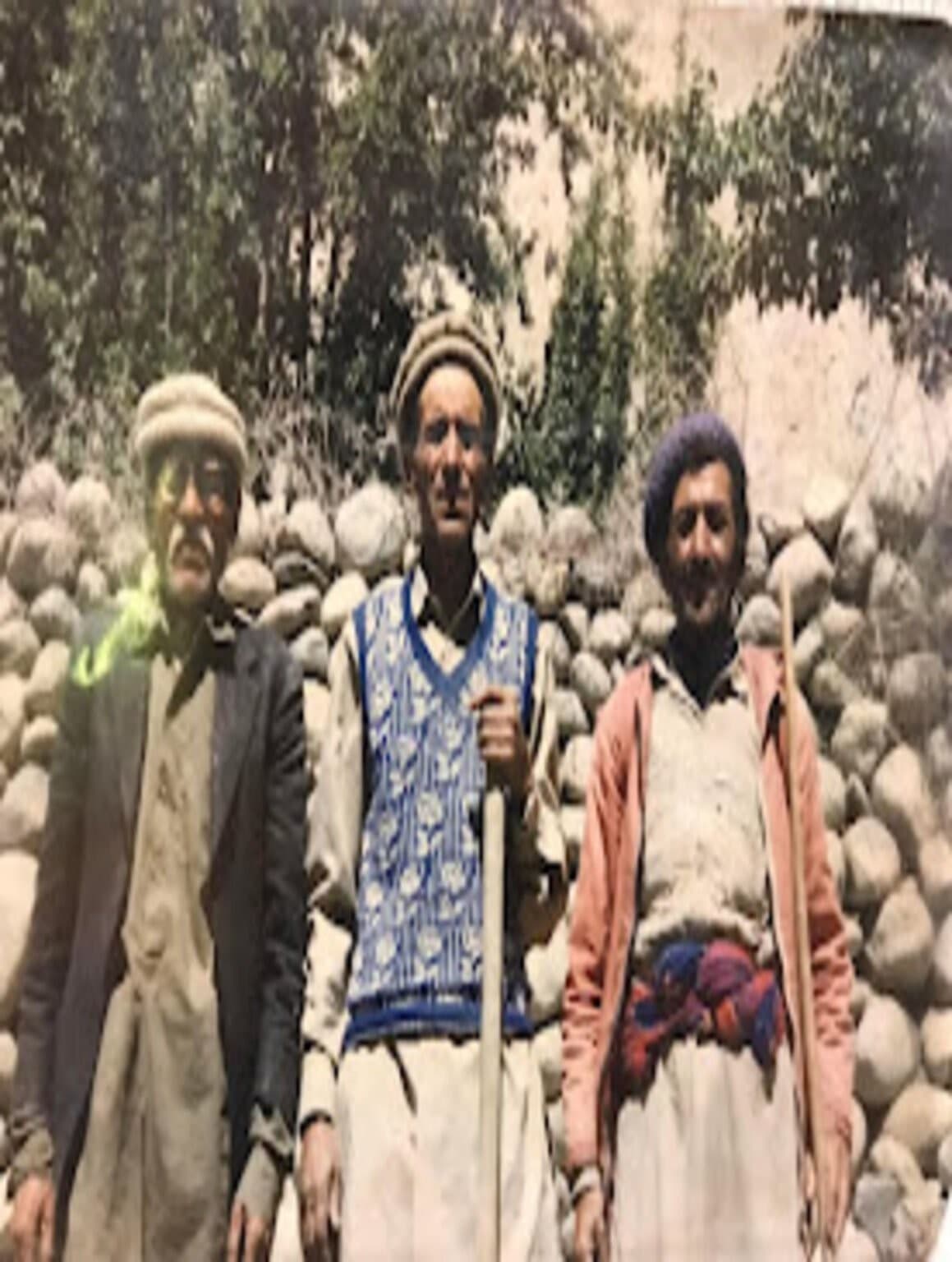 An archival tinted photograph of three men standing by a riverbed with walking sticks