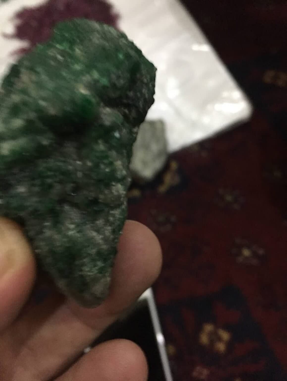 A raw green crystal held in hand under natural daylight