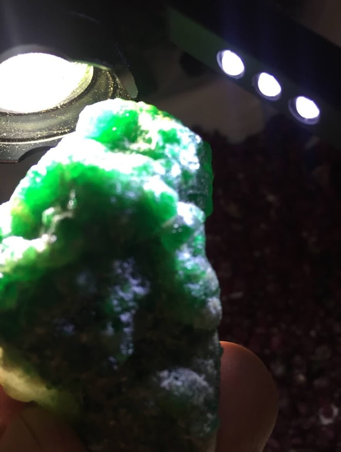 A raw green crystal examined under a jeweler's loupe light