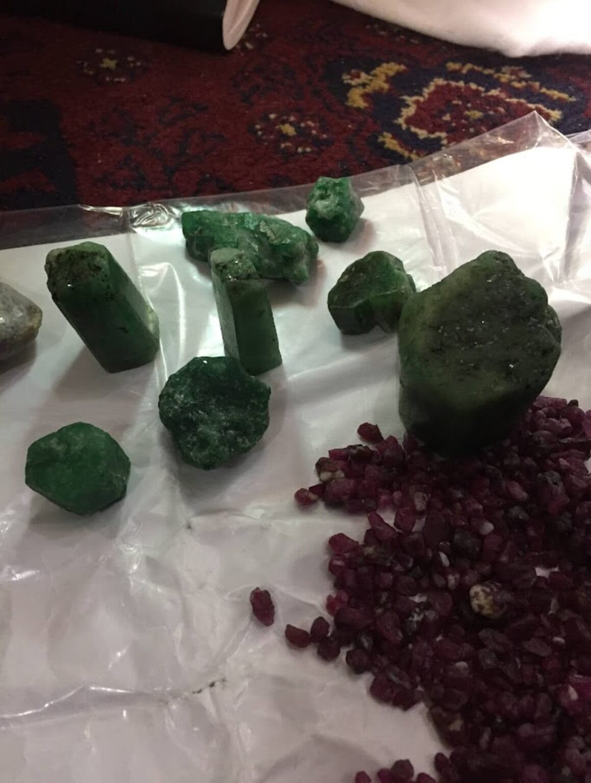 Rough green crystals alongside a pile of raw ruby crystals