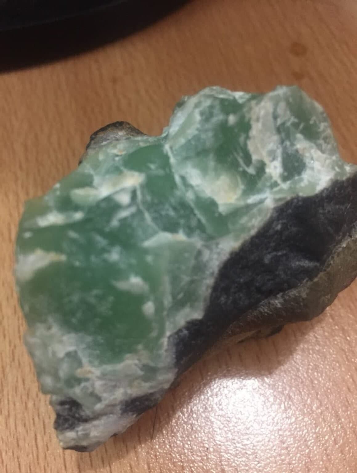 A raw green mineral specimen with dark host rock