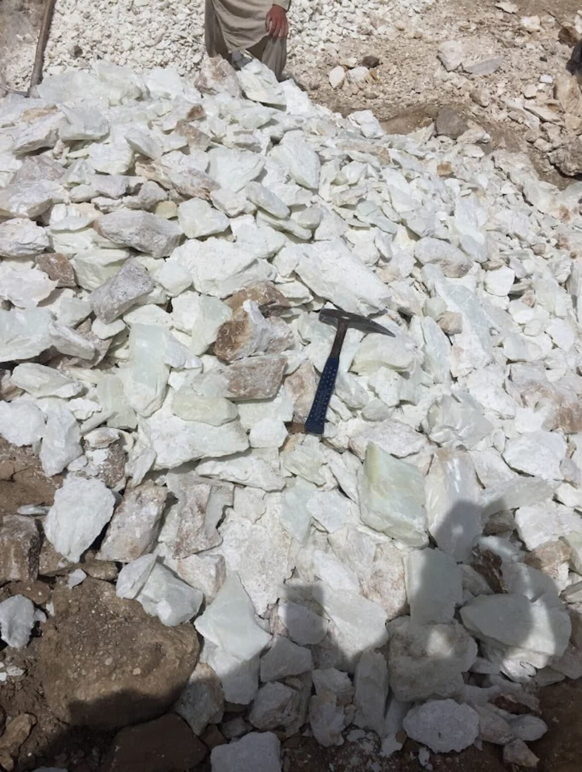 A pile of freshly quarried white stone with a geologist's rock hammer for scale