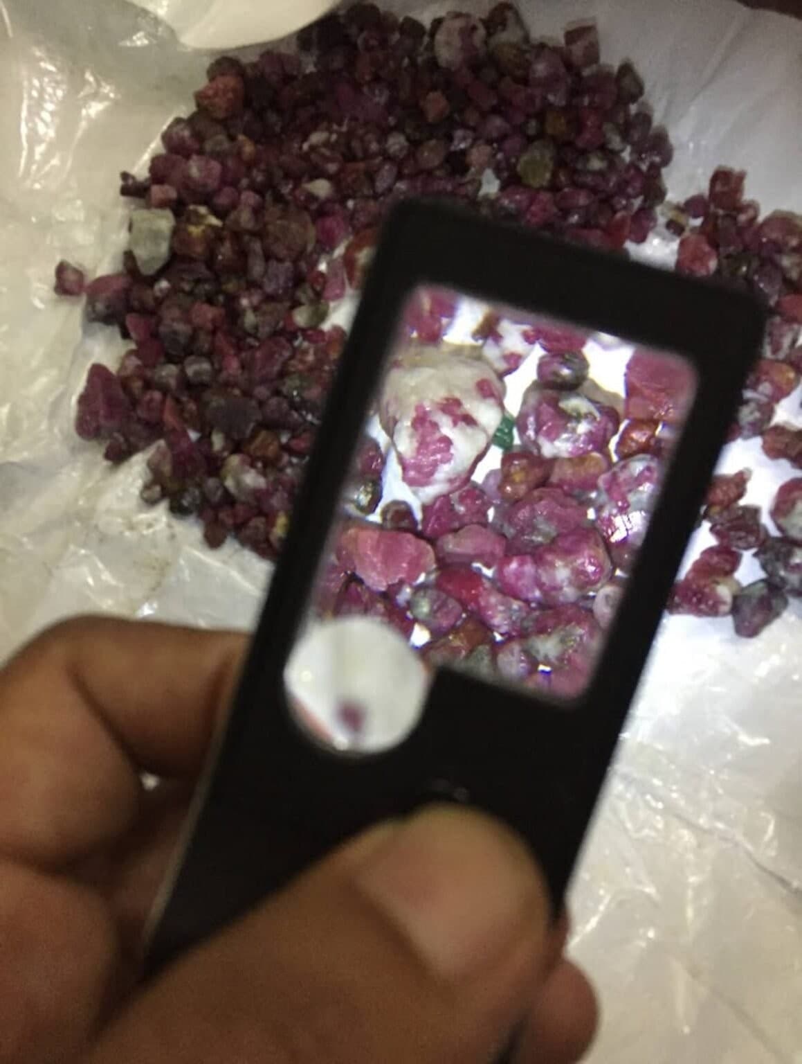 Raw ruby crystals being examined closely with a jeweler's loupe