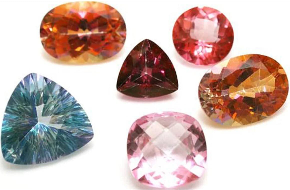 A collection of faceted topaz gemstones in orange, red, blue, and pink
