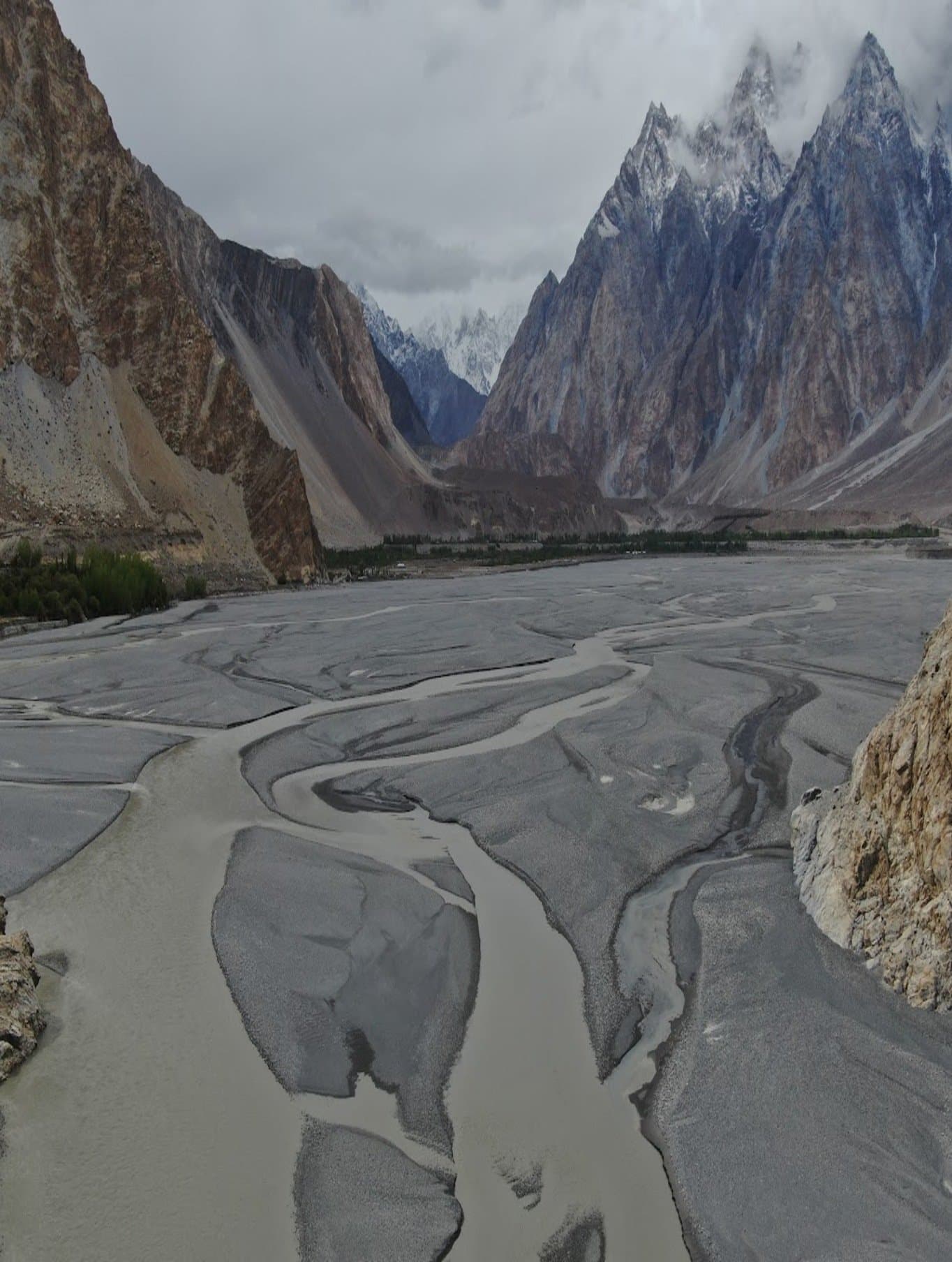 Wide view of a braided glacial river valley beneath the Passu Cones